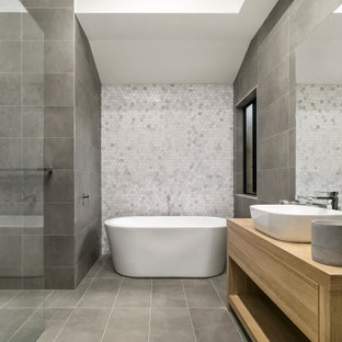 This is an example of a contemporary master bathroom in Melbourne with open cabinets, light wood cabinets, a freestanding tub, an open shower, gray tile, wood benchtops, grey floor, an open shower, a single vanity and a freestanding vanity.
