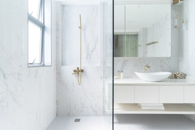 他の地域にあるコンテンポラリースタイルのおしゃれな浴室 (フラットパネル扉のキャビネット、白いキャビネット、白いタイル、石スラブタイル、ベッセル式洗面器、白い床、白い洗面カウンター) の写真