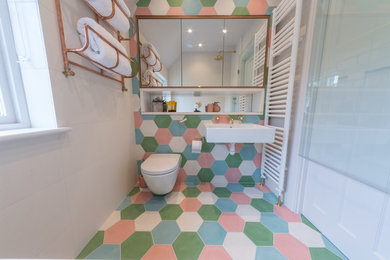 Cette image montre une salle d'eau bohème avec un espace douche bain, WC suspendus, un carrelage bleu, un carrelage vert, un carrelage rose, un carrelage blanc, des carreaux de béton, un mur gris, carreaux de ciment au sol, un lavabo suspendu et un sol multicolore.