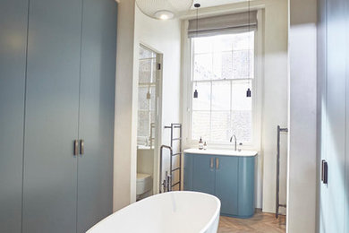 Contemporary ensuite bathroom in London with flat-panel cabinets, blue cabinets, a freestanding bath, a walk-in shower, a wall mounted toilet, beige walls, a built-in sink and a hinged door.