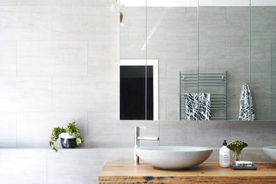 На фото: главная ванная комната в стиле модернизм с отдельно стоящей ванной, серой плиткой, серыми стенами, полом из керамической плитки, настольной раковиной, столешницей из дерева, серым полом и коричневой столешницей