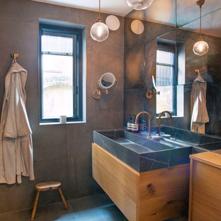 Small eclectic ensuite bathroom in London with flat-panel cabinets, medium wood cabinets, a built-in bath, a shower/bath combination, a wall mounted toilet, brown tiles, ceramic tiles, brown walls, ceramic flooring, marble worktops, grey floors, black worktops and a wall-mounted sink.