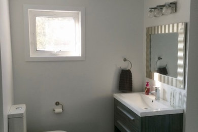 Example of a mid-sized transitional master linoleum floor and gray floor bathroom design in Other with flat-panel cabinets, gray cabinets, a two-piece toilet, white walls, an integrated sink and solid surface countertops