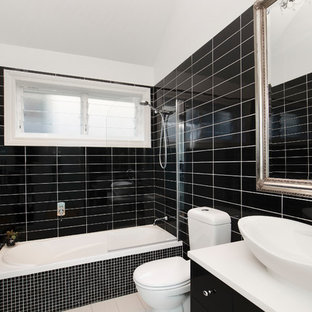 Inspiration for a contemporary 3/4 bathroom in Sydney with flat-panel cabinets, black cabinets, a drop-in tub, a shower/bathtub combo, a two-piece toilet, black tile, black walls, ceramic floors, a vessel sink, solid surface benchtops, white floor, an open shower and white benchtops.