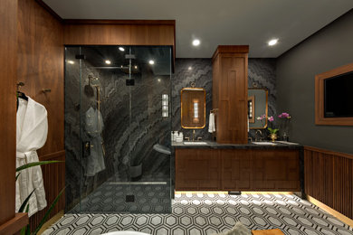 Bathroom - craftsman master black tile and stone slab mosaic tile floor, multicolored floor, double-sink and wall paneling bathroom idea in Calgary with furniture-like cabinets, brown cabinets, a two-piece toilet, gray walls, an undermount sink, marble countertops, a hinged shower door, black countertops and a built-in vanity