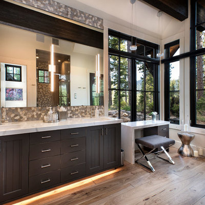 Large mountain style master multicolored tile and pebble tile medium tone wood floor and brown floor bathroom photo in Other with recessed-panel cabinets, dark wood cabinets, white walls, an undermount sink, white countertops and marble countertops