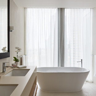 Design ideas for a contemporary master bathroom in Melbourne with flat-panel cabinets, beige cabinets, a freestanding tub, a wall-mount toilet, beige tile, beige walls, an undermount sink, beige floor, a hinged shower door and beige benchtops.
