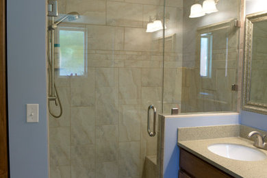 Mid-sized elegant master beige tile and stone slab porcelain tile and beige floor corner shower photo in Salt Lake City with raised-panel cabinets, medium tone wood cabinets, blue walls, an undermount sink, solid surface countertops and a hinged shower door