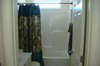 Small 3/4 tub/shower combo photo in Burlington with a drop-in sink, white cabinets, solid surface countertops and a one-piece toilet