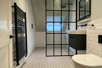 Large modern ensuite wet room bathroom in London with flat-panel cabinets, black cabinets, a two-piece toilet, ceramic tiles, white walls, ceramic flooring, a wall-mounted sink, multi-coloured floors and an open shower.