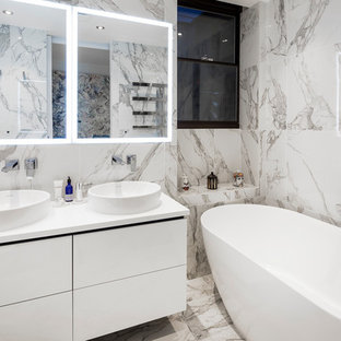 Inspiration for a contemporary bathroom in London with flat-panel cabinets, white cabinets, a freestanding bath, grey tiles, white tiles, marble tiles, white walls, marble flooring, a vessel sink, white floors and white worktops.