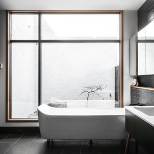 Photo of a mid-sized contemporary master wet room bathroom in Hobart with furniture-like cabinets, black cabinets, a freestanding tub, black tile, black walls, an undermount sink, black floor, white benchtops, a one-piece toilet, ceramic tile, ceramic floors, laminate benchtops and an open shower.