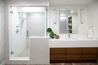 This is an example of a modern ensuite bathroom in Calgary with flat-panel cabinets, brown cabinets, a built-in bath, a corner shower, a one-piece toilet, white tiles, mosaic tiles, white walls, porcelain flooring, a submerged sink, solid surface worktops, brown floors, a hinged door and white worktops.