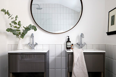 This is an example of a scandi family bathroom in London with a shower/bath combination, white tiles, ceramic tiles, white walls, ceramic flooring, a wall-mounted sink, black floors, freestanding cabinets and grey cabinets.