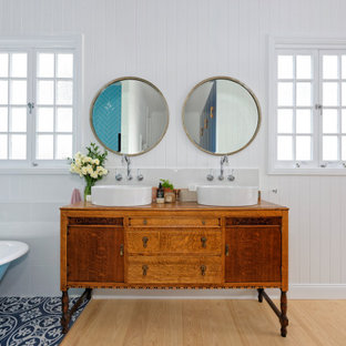 Design ideas for a tropical bathroom in Brisbane with flat-panel cabinets, medium wood cabinets, a claw-foot tub, gray tile, white walls, light hardwood floors, a vessel sink, wood benchtops, beige floor, brown benchtops, a double vanity, a freestanding vanity and planked wall panelling.
