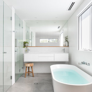 Inspiration for a mid-sized contemporary master bathroom in Perth with furniture-like cabinets, white cabinets, a freestanding tub, white tile, ceramic tile, white walls, porcelain floors, an integrated sink, grey floor, white benchtops, a curbless shower and a hinged shower door.