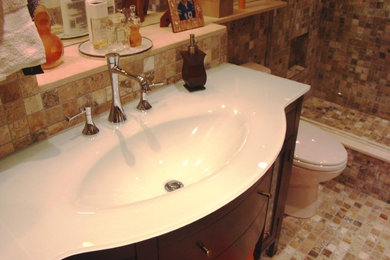 Immagine di una stanza da bagno design con lavabo integrato, ante lisce, ante in legno bruno, top in vetro, doccia aperta, WC monopezzo e piastrelle multicolore