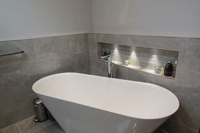 Bild på ett mellanstort funkis grå grått en-suite badrum, med grå skåp, ett fristående badkar, en öppen dusch, en vägghängd toalettstol, grå kakel, grå väggar, ett integrerad handfat och med dusch som är öppen