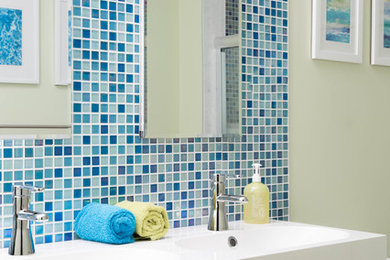 Mid-sized minimalist kids' blue tile and glass tile ceramic tile tub/shower combo photo in Philadelphia with flat-panel cabinets, light wood cabinets, green walls, an integrated sink and solid surface countertops