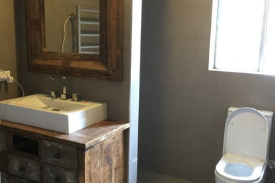 Cette image montre une salle de bain chalet en bois brun de taille moyenne avec une douche ouverte, WC séparés, un carrelage gris, des carreaux de porcelaine, un mur gris, un sol en carrelage de porcelaine, une vasque et un plan de toilette en bois.