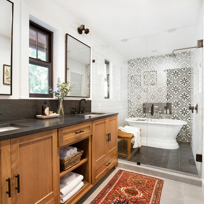 Farmhouse master black and white tile gray floor bathroom photo in Seattle with shaker cabinets, medium tone wood cabinets, white walls, an undermount sink, a hinged shower door and black countertops