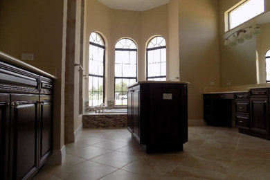 Large traditional ensuite bathroom in Tampa with raised-panel cabinets, dark wood cabinets, an alcove bath, beige tiles, glass tiles, beige walls, limestone flooring, a submerged sink and beige floors.