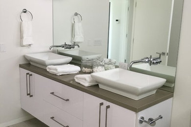 Photo of a medium sized contemporary shower room bathroom in Los Angeles with flat-panel cabinets, white cabinets, a one-piece toilet, white walls, porcelain flooring, a vessel sink, solid surface worktops and beige floors.