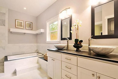 Cette photo montre une grande salle de bain principale chic avec un placard à porte shaker, des portes de placard blanches, une baignoire posée, un carrelage gris, des carreaux de porcelaine, un mur gris et un lavabo encastré.