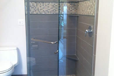 Corner shower - small transitional 3/4 gray tile and porcelain tile porcelain tile and gray floor corner shower idea in Seattle with flat-panel cabinets, brown cabinets, a one-piece toilet, gray walls, quartz countertops and a hinged shower door