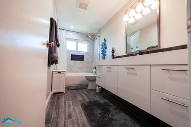 Medium sized modern ensuite bathroom in Los Angeles with flat-panel cabinets, white cabinets, an alcove bath, a shower/bath combination, white tiles, marble tiles, white walls, laminate floors, grey floors, a shower curtain, white worktops, a two-piece toilet, an integrated sink and solid surface worktops.