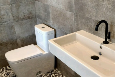 サンディエゴにある高級な中くらいなインダストリアルスタイルのおしゃれなバスルーム (浴槽なし) (一体型トイレ	、グレーの壁、セラミックタイルの床、壁付け型シンク、シェーカースタイル扉のキャビネット、ヴィンテージ仕上げキャビネット、グレーのタイル、セメントタイル、マルチカラーの床) の写真