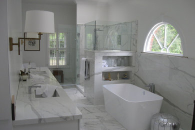 セントルイスにあるラグジュアリーな巨大なトラディショナルスタイルのおしゃれなマスターバスルーム (アンダーカウンター洗面器、シェーカースタイル扉のキャビネット、白いキャビネット、大理石の洗面台、置き型浴槽、アルコーブ型シャワー、分離型トイレ、白いタイル、石タイル、白い壁、大理石の床、白い床、開き戸のシャワー) の写真