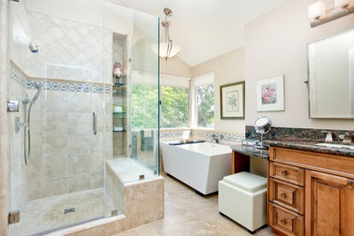 Example of a mid-sized trendy master beige tile and stone tile travertine floor and beige floor bathroom design in Orange County with raised-panel cabinets, light wood cabinets, beige walls, an undermount sink, granite countertops and a hinged shower door