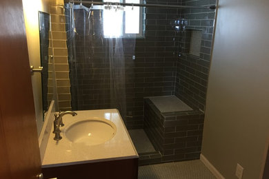 Inspiration for a small modern master gray tile and glass tile mosaic tile floor doorless shower remodel in Indianapolis with an integrated sink, raised-panel cabinets, medium tone wood cabinets, quartz countertops, a two-piece toilet and gray walls