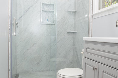 Example of a large transitional master stone slab marble floor and gray floor bathroom design in Other with raised-panel cabinets, gray cabinets, a one-piece toilet, blue walls, an integrated sink, solid surface countertops and white countertops