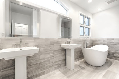 ニューヨークにあるコンテンポラリースタイルのおしゃれなマスターバスルーム (置き型浴槽、グレーのタイル、石タイル、白い壁、大理石の床、ペデスタルシンク) の写真