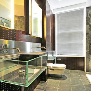 This is an example of a medium sized urban bathroom in London with a wall mounted toilet, a wall-mounted sink, grey floors, a corner shower, grey tiles and black walls.