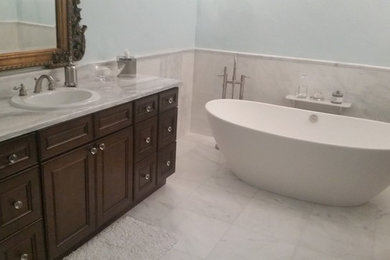Photo of a large traditional ensuite bathroom in Tampa with recessed-panel cabinets, brown cabinets, a freestanding bath, a corner shower, a two-piece toilet, white tiles, marble tiles, blue walls, marble flooring, a built-in sink, marble worktops, white floors, a hinged door and white worktops.