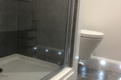 Photo of a small modern shower room bathroom in Essex with grey tiles, white cabinets, a built-in shower, a wall mounted toilet, ceramic tiles, white walls, ceramic flooring and a wall-mounted sink.