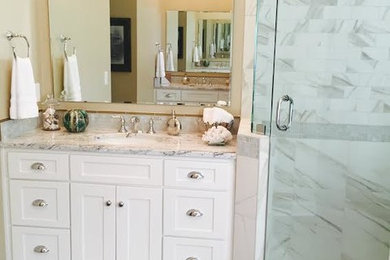 Inspiration for a mid-sized transitional master white tile and porcelain tile porcelain tile and brown floor bathroom remodel in Other with an undermount sink, recessed-panel cabinets, white cabinets, granite countertops, a one-piece toilet, beige walls, a hinged shower door and multicolored countertops