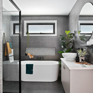 Photo of a small contemporary master bathroom in Other with a freestanding tub, a corner shower, gray tile, ceramic tile, ceramic floors, grey floor, a hinged shower door, flat-panel cabinets, grey cabinets, a vessel sink, laminate benchtops and white benchtops.