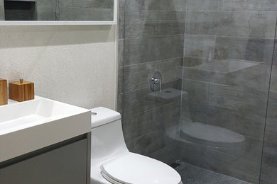 他の地域にある低価格の小さなモダンスタイルのおしゃれな浴室 (グレーのキャビネット、オープン型シャワー、一体型トイレ	、グレーのタイル、磁器タイル、白い壁、セラミックタイルの床、一体型シンク、珪岩の洗面台) の写真