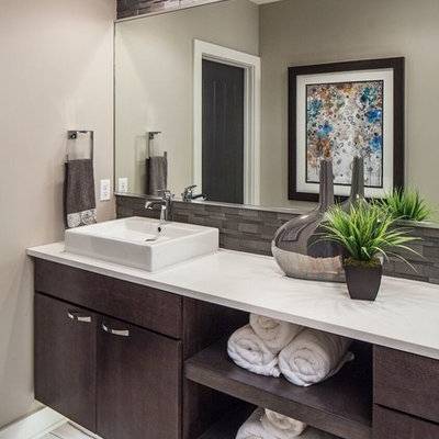 Trendy master brown tile freestanding bathtub photo in Omaha with flat-panel cabinets, dark wood cabinets, gray walls, a vessel sink and white countertops