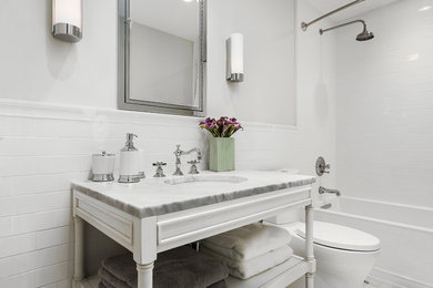 Идея дизайна: ванная комната в стиле неоклассика (современная классика) с врезной раковиной, фасадами островного типа, белыми фасадами, мраморной столешницей, ванной в нише, душем над ванной, раздельным унитазом, белой плиткой и керамической плиткой