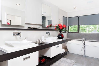 Exempel på ett mellanstort modernt en-suite badrum, med släta luckor, vita skåp, ett fristående badkar, en öppen dusch, en toalettstol med hel cisternkåpa, grå kakel, porslinskakel, grå väggar, klinkergolv i porslin, ett fristående handfat och träbänkskiva