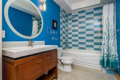 バンクーバーにあるお手頃価格の中くらいなビーチスタイルのおしゃれなバスルーム (浴槽なし) (フラットパネル扉のキャビネット、濃色木目調キャビネット、アルコーブ型浴槽、シャワー付き浴槽	、分離型トイレ、青いタイル、マルチカラーのタイル、白いタイル、セラミックタイル、青い壁、コンクリートの床、一体型シンク、グレーの床、シャワーカーテン) の写真