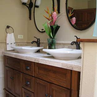 Esempio di una stanza da bagno tropicale di medie dimensioni con lavabo a bacinella, ante in legno bruno, top piastrellato, vasca ad alcova, vasca/doccia, WC a due pezzi, piastrelle beige, piastrelle in pietra, pareti beige, pavimento in travertino e ante con riquadro incassato
