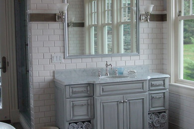 Medium sized classic ensuite bathroom in Boston with raised-panel cabinets, grey cabinets, a freestanding bath, a two-piece toilet, white tiles, metro tiles, white walls, medium hardwood flooring, a submerged sink, marble worktops and grey floors.