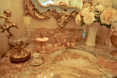 Modelo de cuarto de baño tradicional con armarios tipo mueble, puertas de armario marrones, paredes beige, suelo de madera en tonos medios, lavabo encastrado, encimera de mármol, suelo marrón y encimeras beige