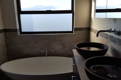 Exemple d'une salle de bain principale tendance en bois foncé de taille moyenne avec une baignoire indépendante, un carrelage beige, un carrelage de pierre, un mur beige, un sol en carrelage de porcelaine, une vasque et un plan de toilette en calcaire.
